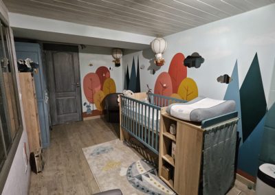 Photo montrant la partie droite de la chambre d'un bébé. Peinture murale au thème de la forêt.
