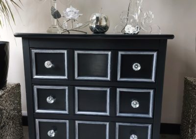 Un mobilier restauré dans une couleur noir avec des poignées en verre.